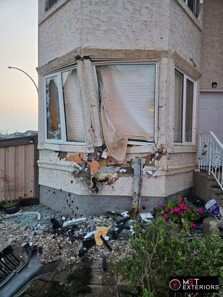 Close view of vehicle collision damage to stucco, sheathing and a bay window before insurance restoration