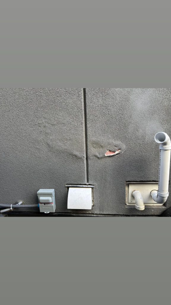 Damaged grey stucco near furnace exhaust vent on an Edmonton exterior wall