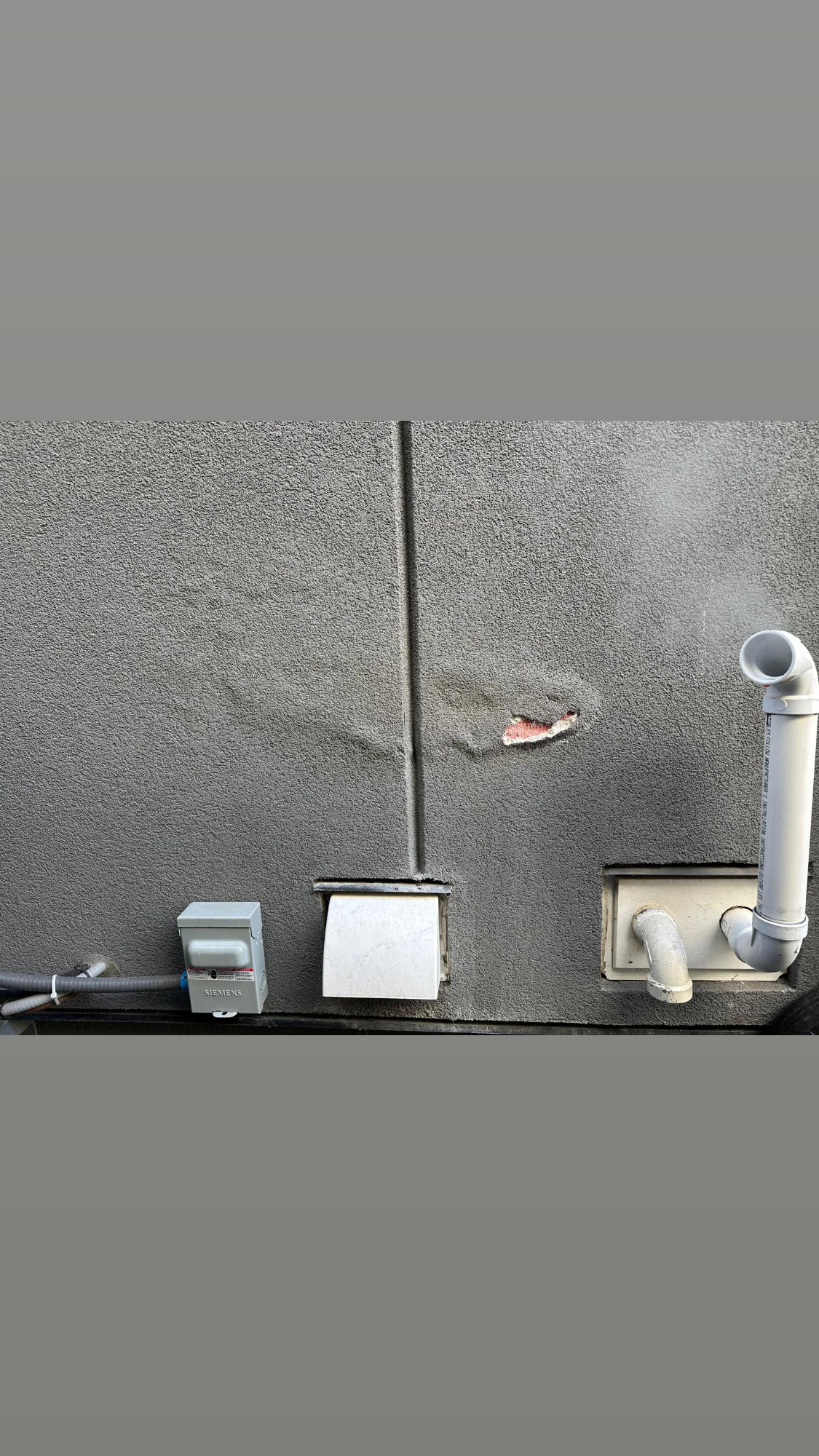 Close-up of localized damage on grey stucco wall near furnace exhaust piping