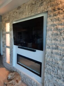 Silver travertine split-face stone feature wall surrounding television and modern fireplace in Edmonton home
