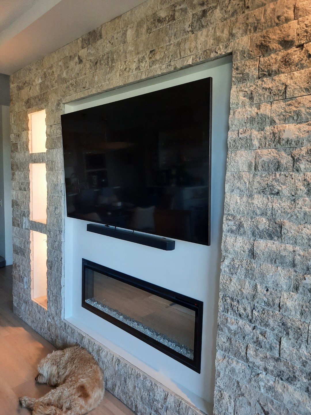 Silver travertine split-face stone feature wall surrounding television and modern fireplace in Edmonton home