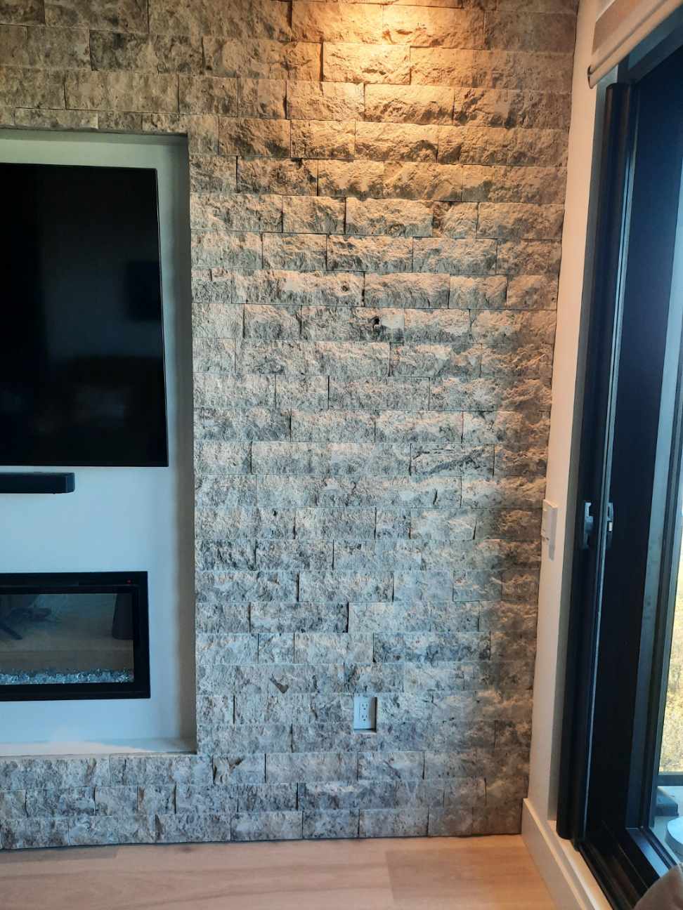 Close-up of silver travertine split-face stone cladding beside a modern fireplace