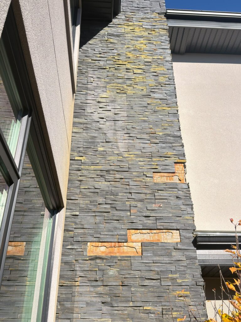 Exterior stacked stone veneer with missing pieces exposing the underlying surface