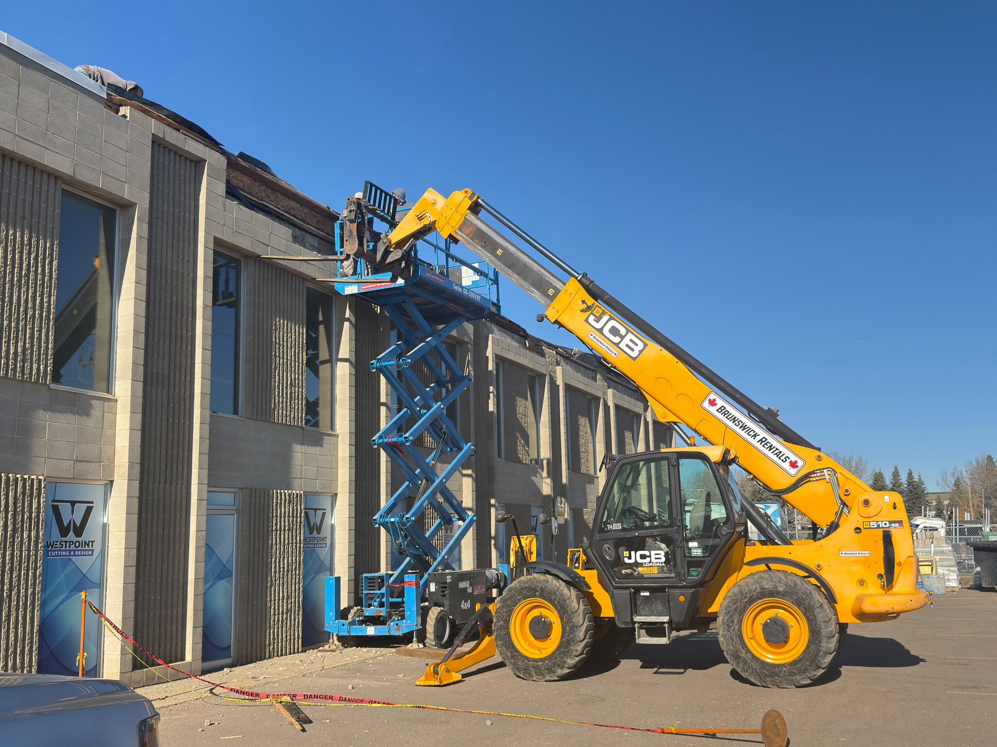 Telehandler and elevated work platform beside a two-storey commercial masonry facade
