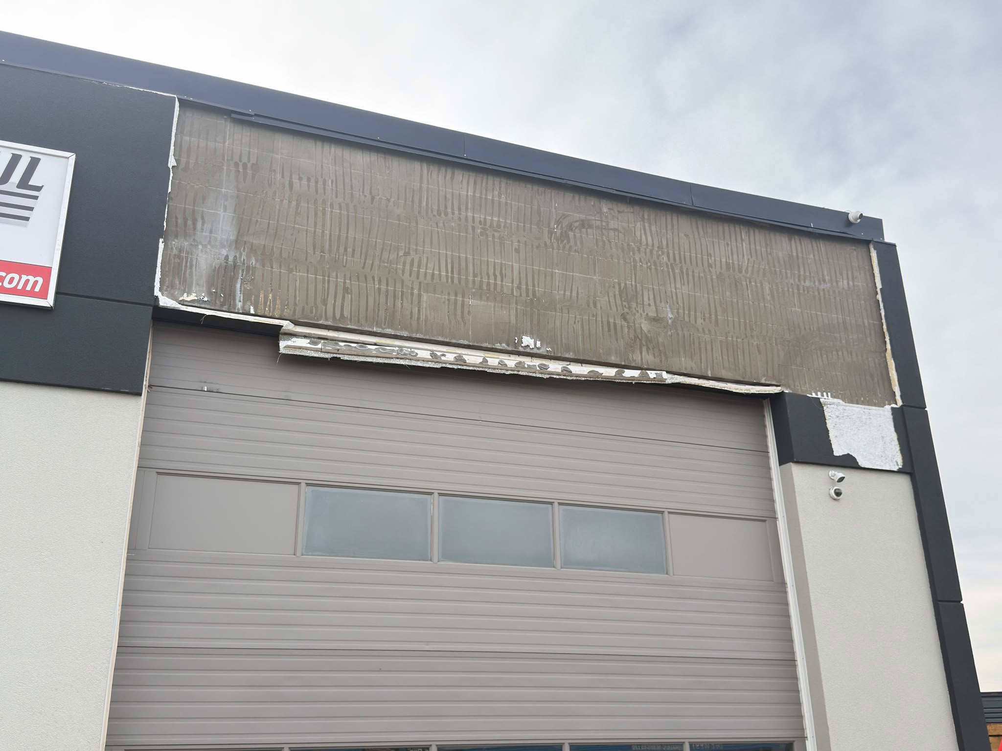 Commercial garage facade with a wide strip of exterior cladding missing above an overhead door